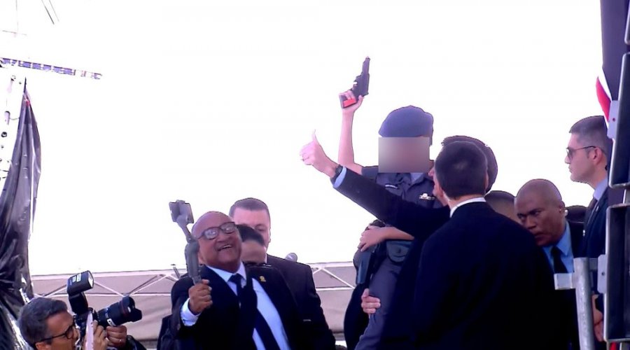 [Em formatura militar, Bolsonaro posa pra foto com criança apontando arma de brinquedo pro alto ]